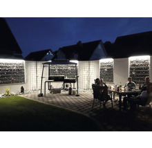 Abendliche Gartenszene mit Grill, Gabionenwänden und sitzenden Personen
