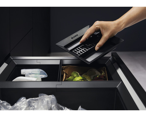 Une personne place une poubelle de cuisine Blanco dans un meuble coulissant avec un système de tri des déchets