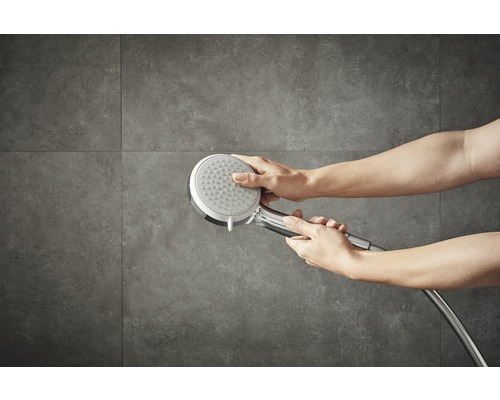 Une douchette est tenue par des mains sur un fond gris.