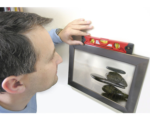 Une personne ajuste un tableau encadré avec un niveau à bulle.