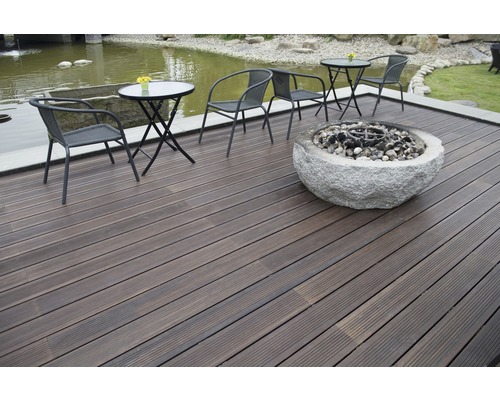 Terrasse mit dunklen Holzdielen, Sitzgruppe und Feuerstelle aus Stein.