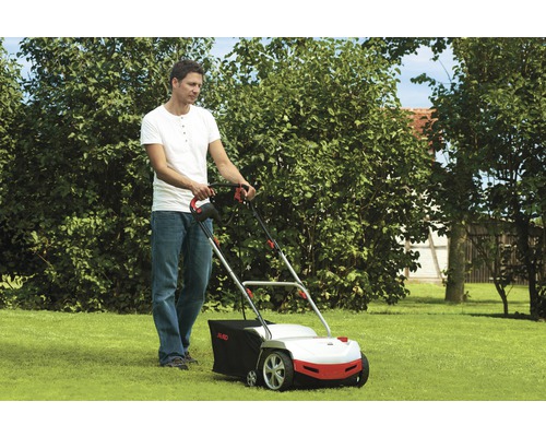 Un homme utilise un scarificateur à gazon dans le jardin.