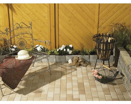 Gestalteter Gartenbereich mit Sitzgelegenheit, Feuerstelle und Holzstapel auf Pflastersteinen