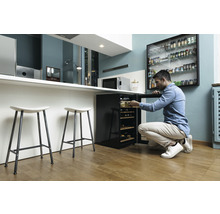 Un homme ouvre un réfrigérateur à vin dans une cuisine moderne avec des tabourets de bar