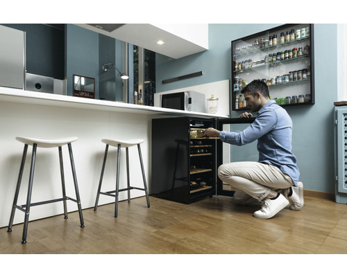Mann öffnet einen Weinkühlschrank in einer modernen Küche mit Barhockern
