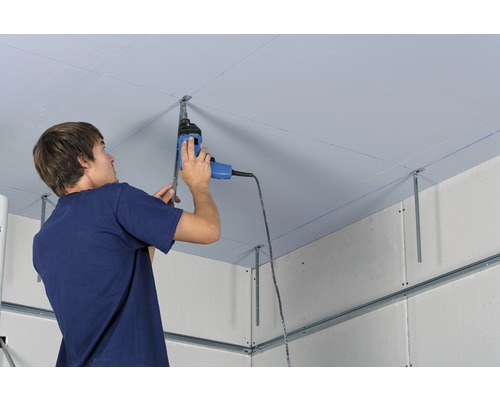 Un homme installe un revêtement de plafond avec une perceuse sur une structure métallique.