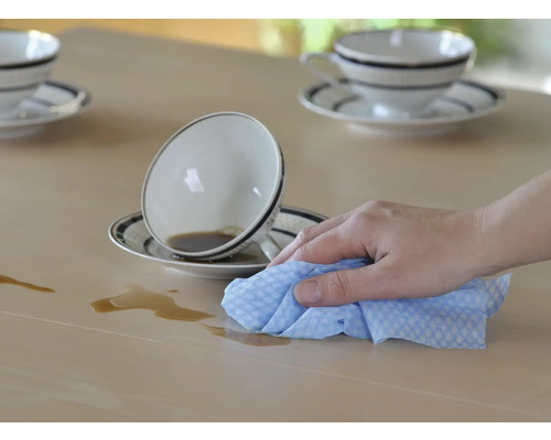Une main essuie un liquide renversé sur une table avec un chiffon.