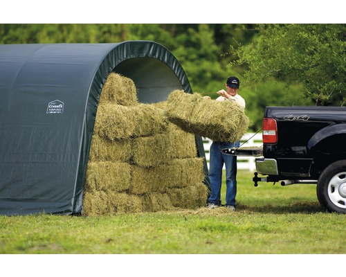 Heulager mit Mann beim Aufladen von Heuballen auf einen Lastwagen