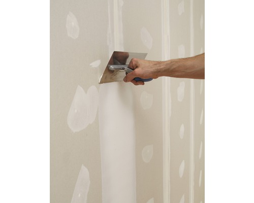 Une personne lisse du plâtre avec une spatule sur une plaque de plâtre.