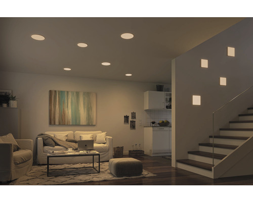 Wohnzimmer mit Deckenleuchten und Wandleuchten neben Treppe