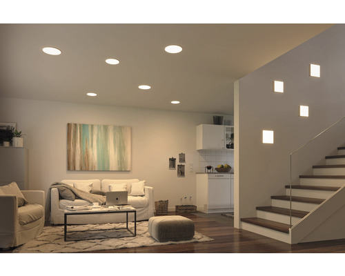 Wohnzimmer mit Deckeneinbauleuchten und Wandleuchten neben einer Treppe