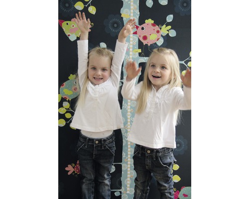 Deux filles se tiennent devant une toise pour enfants avec des motifs d''oiseaux sur un mur sombre avec des motifs floraux.