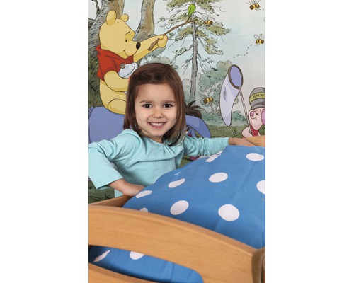 Fille dans un lit devant un papier peint à motif Winnie l''ourson.