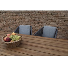 Scène de mobilier de jardin avec table en bois, deux chaises avec coussins et une corbeille de fruits devant un mur de briques
