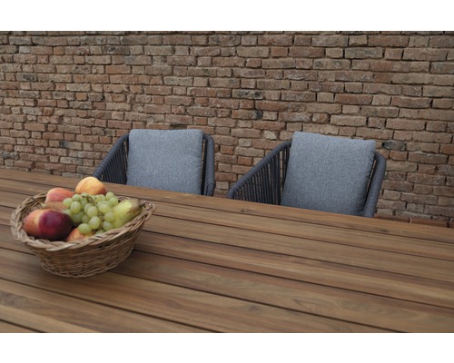 Gartenmöbel-Szene mit Holztisch, zwei Stühlen mit Kissen und einem Obstkorb vor einer Backsteinmauer