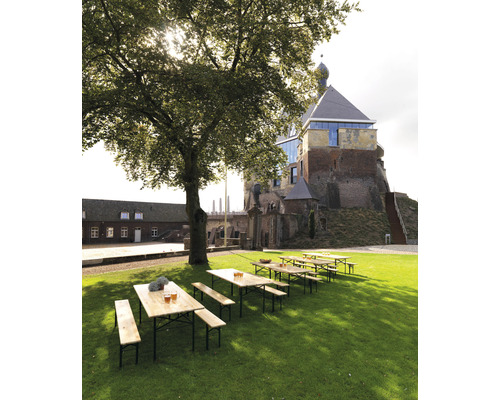 Scène avec des tables de brasserie et des bancs sur une pelouse devant un bâtiment historique