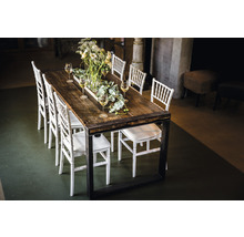 Table de salle à manger avec plateau en bois, cadre en métal et chaises blanches, décorée de fleurs et de verres à vin.
