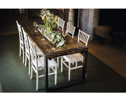 Table de salle à manger avec plateau en bois, cadre en métal et chaises blanches, décorée de fleurs et de verres à vin.