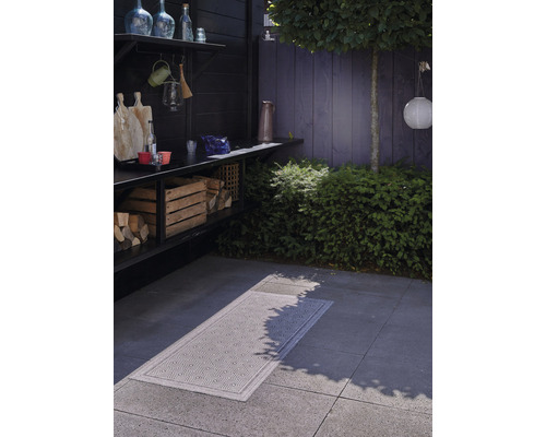 Espace extérieur avec stockage de bois, plan de travail et tapis à motifs sur le sol.