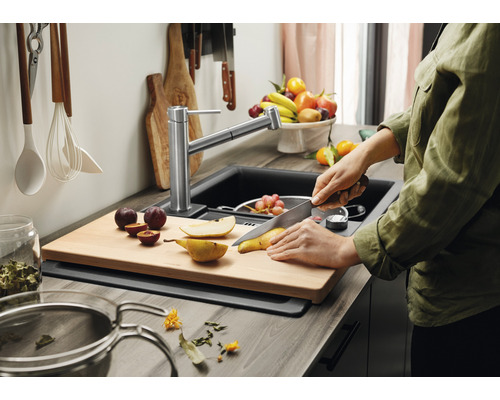 Küchenszene mit Spüle, Armatur und Person, die Obst auf einem Schneidebrett schneidet.