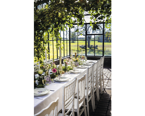 Table dressée de manière festive avec des chaises blanches dans une serre pour une célébration