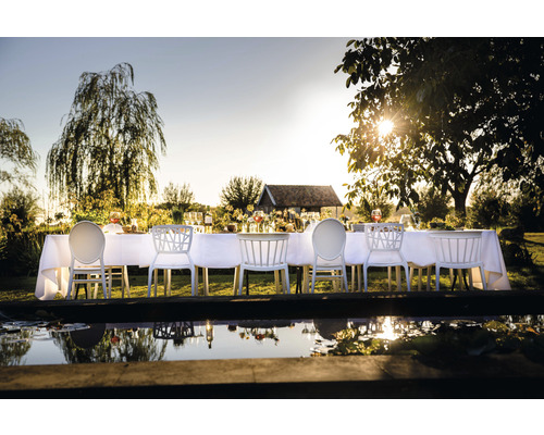 Table à manger dressée pour une fête avec des chaises blanches dans le jardin