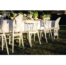 Scène avec mobilier de jardin : table avec une nappe blanche et des chaises sur une pelouse.