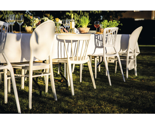 Scène avec mobilier de jardin : table avec une nappe blanche et des chaises sur une pelouse.