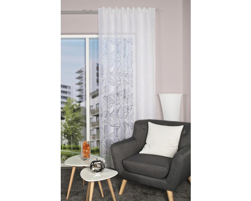 Salon avec fauteuil, tables d''appoint et rideaux à motif de feuilles devant la fenêtre