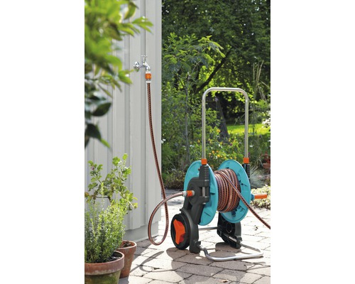 Gartenszene mit einem Gartenschlauchwagen mit Schlauchanschluss an einem Wasserhahn
