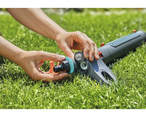 Eine Person verbindet einen Gartenschlauchanschluss mit einem Rasensprenger.