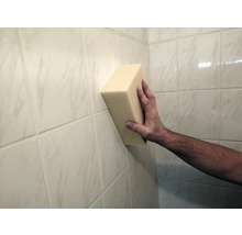 Eine Hand hält einen Schwamm an eine geflieste Wand.
