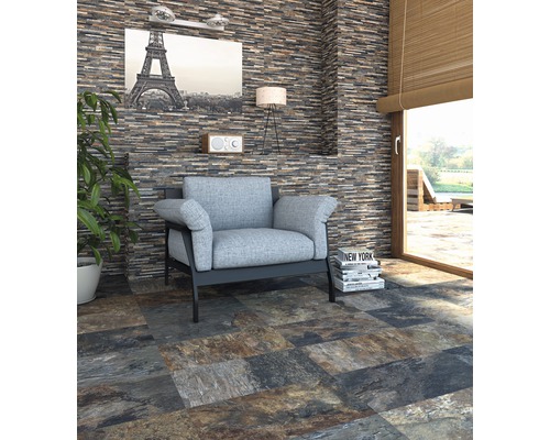 Wohnzimmer mit Natursteinmauer und Bodenfliesen in Steinoptik, Sessel und Dekoration