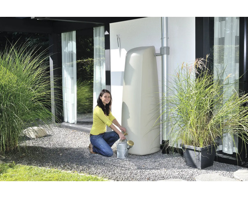 Frau befüllt eine Giesskanne an einem stehenden Wassertank im Garten.