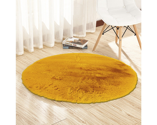 Runder, gelber Teppich aus Kunstfell auf Holzboden neben einem Stuhl
