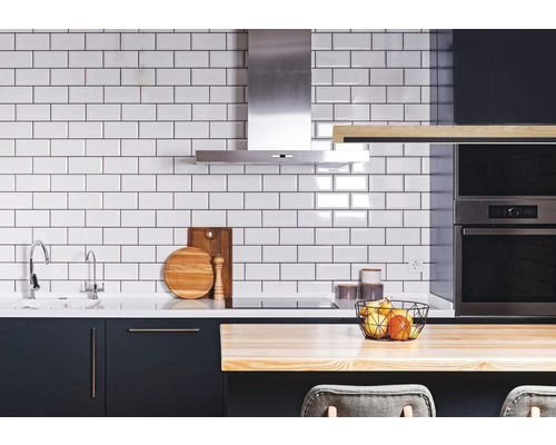 Cuisine claire avec carrelage blanc, hotte aspirante, évier et ustensiles de cuisine.