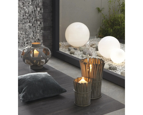 Scène décorative avec lanterne, coussin, photophores en brindilles et boules de jardin sur gravier