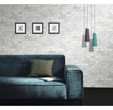 Wohnzimmer mit Sofa, Kissen, Bildern und Pendelleuchten vor einer gemusterten Ziegelwand