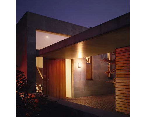 Entrée de maison éclairée avec maison en bois et mur en pierre au crépuscule.
