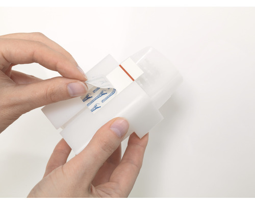 Eine Person entfernt die Schutzfolie von einem Befestigungsstreifen an einem Gerät.