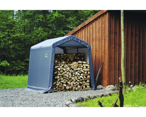 Hangar de stockage gris avec pile de bois à l''extérieur.