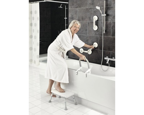 Ältere Frau steigt mit Badewannen-Einstiegshilfe und Tritthocker in eine Badewanne in einem Badezimmer