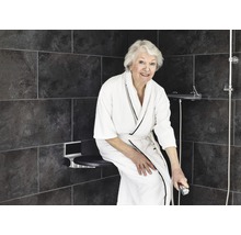 Femme assise sur un siège de douche dans une douche à l''italienne avec des carreaux gris.