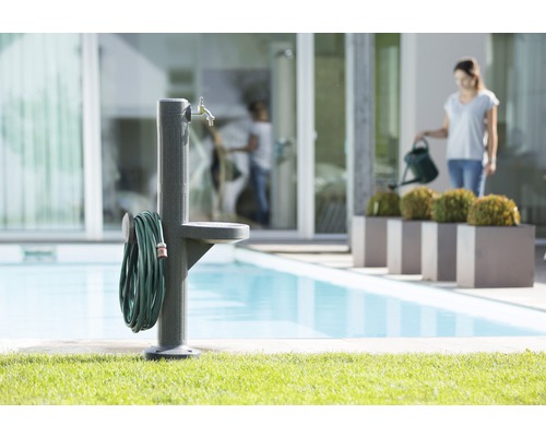 Scène de jardin avec borne fontaine, tuyau d''arrosage et femme avec arrosoir