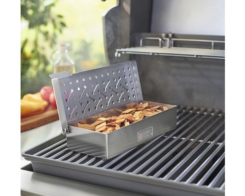 Barbecue avec boîte à fumer remplie de bois à fumer sur une grille de cuisson