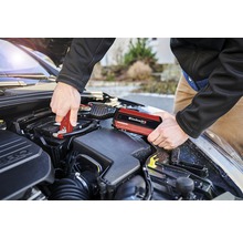 Ein Mann schliesst mit einer roten Starthilfe von Einhell eine Autobatterie an.