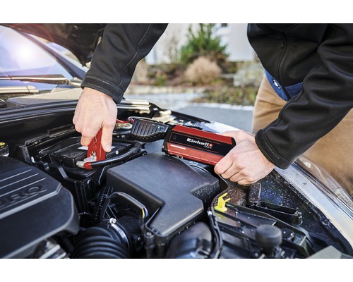 Ein Mann schliesst mit einer roten Starthilfe von Einhell eine Autobatterie an.