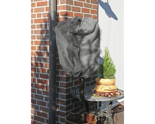 Pflanze mit Winterschutzhaube auf einem Gartentisch vor einer Backsteinmauer