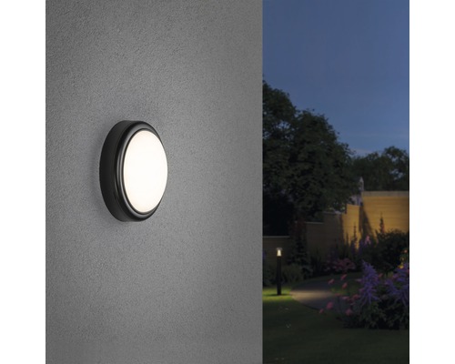 Applique murale extérieure ronde éclairée sur un mur avec jardin en arrière-plan