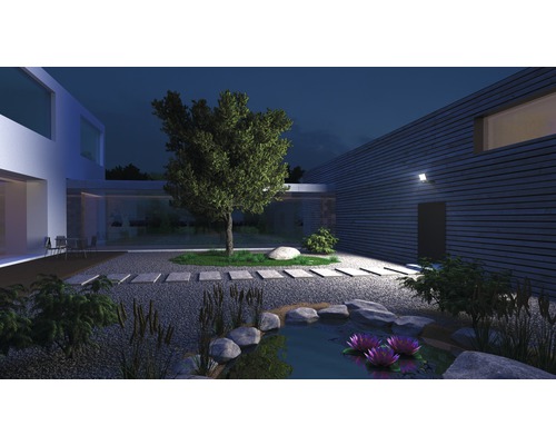 Beleuchteter Garten mit Teich, Steinen, Pflanzen und modernem Haus bei Nacht.